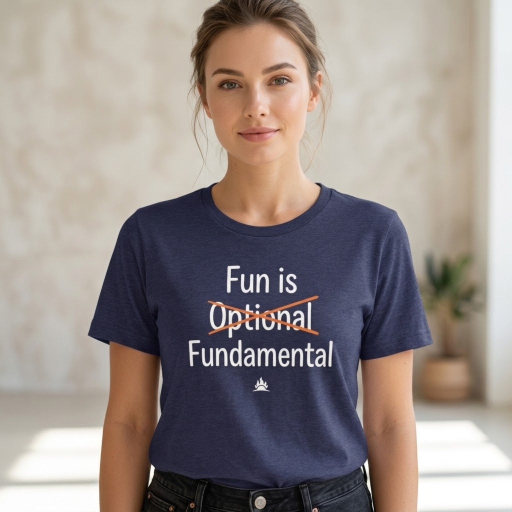A woman wearing a navy blue graphic t-shirt with the text 'Fun is Optional Fundamental' printed on the front, with 'Optional' crossed out in red. The background is a softly blurred indoor setting.