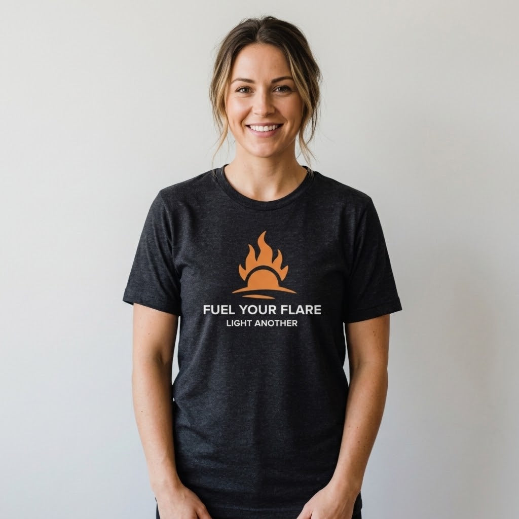 A smiling woman wearing a dark heather gray t-shirt with an orange flame graphic and the text 'FUEL YOUR FLARE LIGHT ANOTHER' printed on the chest, set against a plain light gray background.