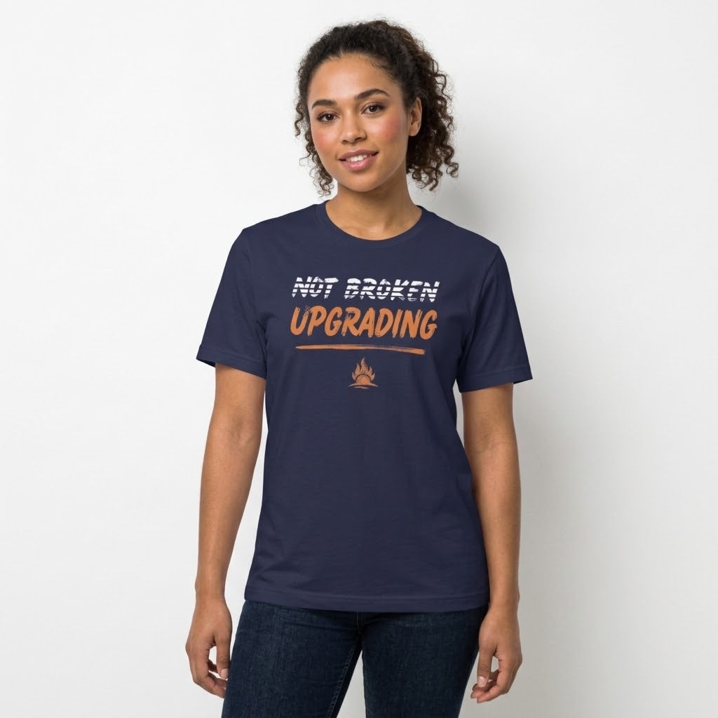 A woman modeling a navy blue t-shirt with a graphic that reads 'NOT BROKEN UPGRADING' in white and orange text, paired with dark blue jeans, against a plain white background.