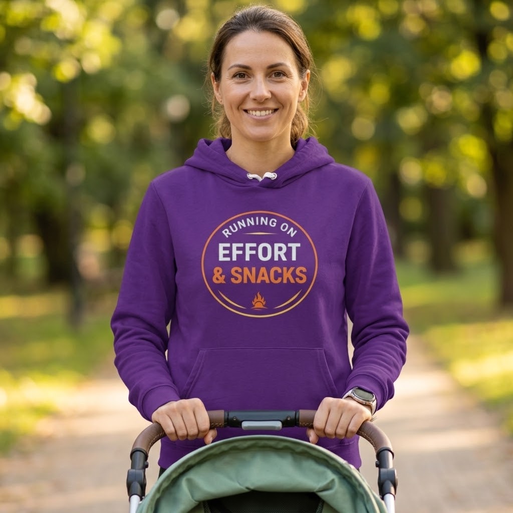 A woman wearing a purple hoodie with a circular graphic that reads 'RUNNING ON EFFORT & SNACKS' stands in a park pushing a stroller.