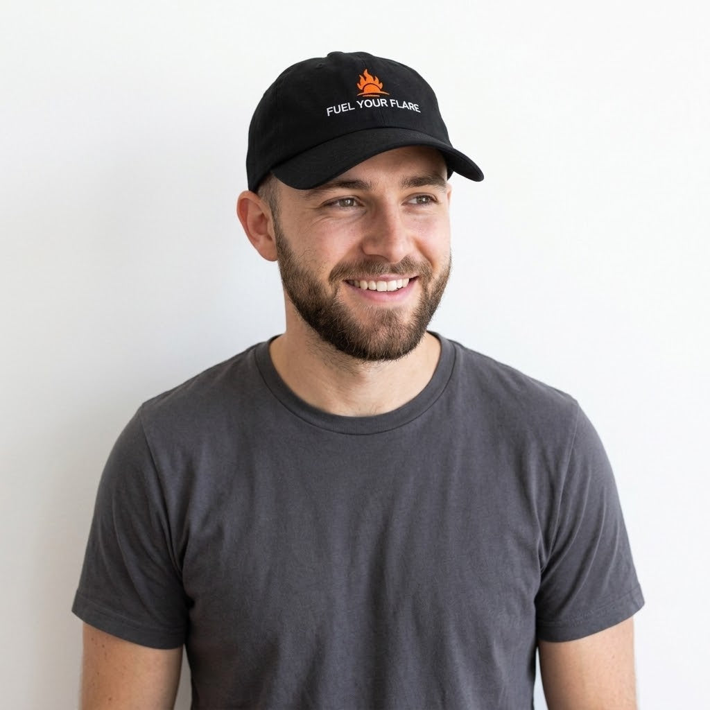 A smiling man wearing a black baseball cap with a small orange flame logo and the text 'FUEL YOUR FLAME' in white, paired with a dark gray t-shirt against a plain white background.