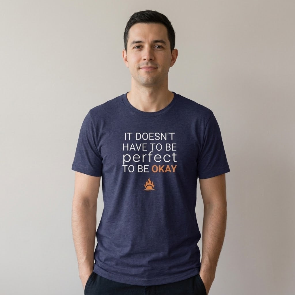 A man wearing a navy blue heather t-shirt with the text 'IT DOESN'T HAVE TO BE perfect TO BE OKAY' in white and orange, along with an orange flare graphic, against a plain light gray background.