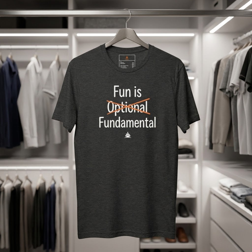A dark heather gray graphic t-shirt hanging on a wooden hanger in a modern, well-lit closet or retail display. The shirt features the text 'Fun is Optional Fundamental' in white, with the word 'Optional' crossed out in orange.
