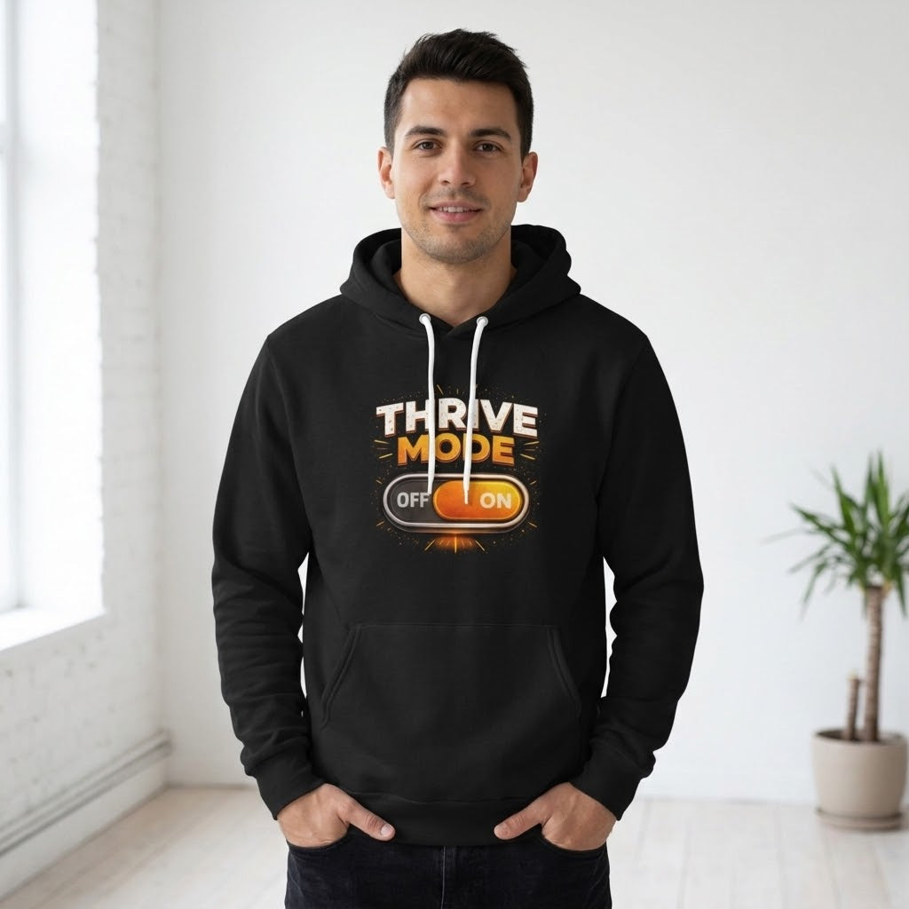 A man wearing a black pullover hoodie with a graphic that reads 'THRIVE MODE OFF ON' in white and orange-yellow text, standing in a bright, modern room with a potted plant in the background.