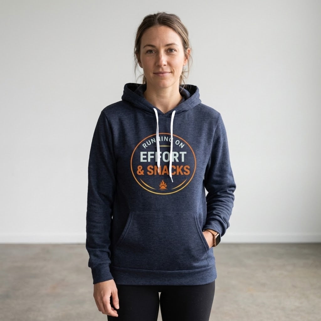 A woman wearing a navy blue heather hoodie with a circular graphic on the chest that reads 'RUNNING ON EFFORT & SNACKS' in orange and white, paired with black leggings, standing against a plain light gray wall.